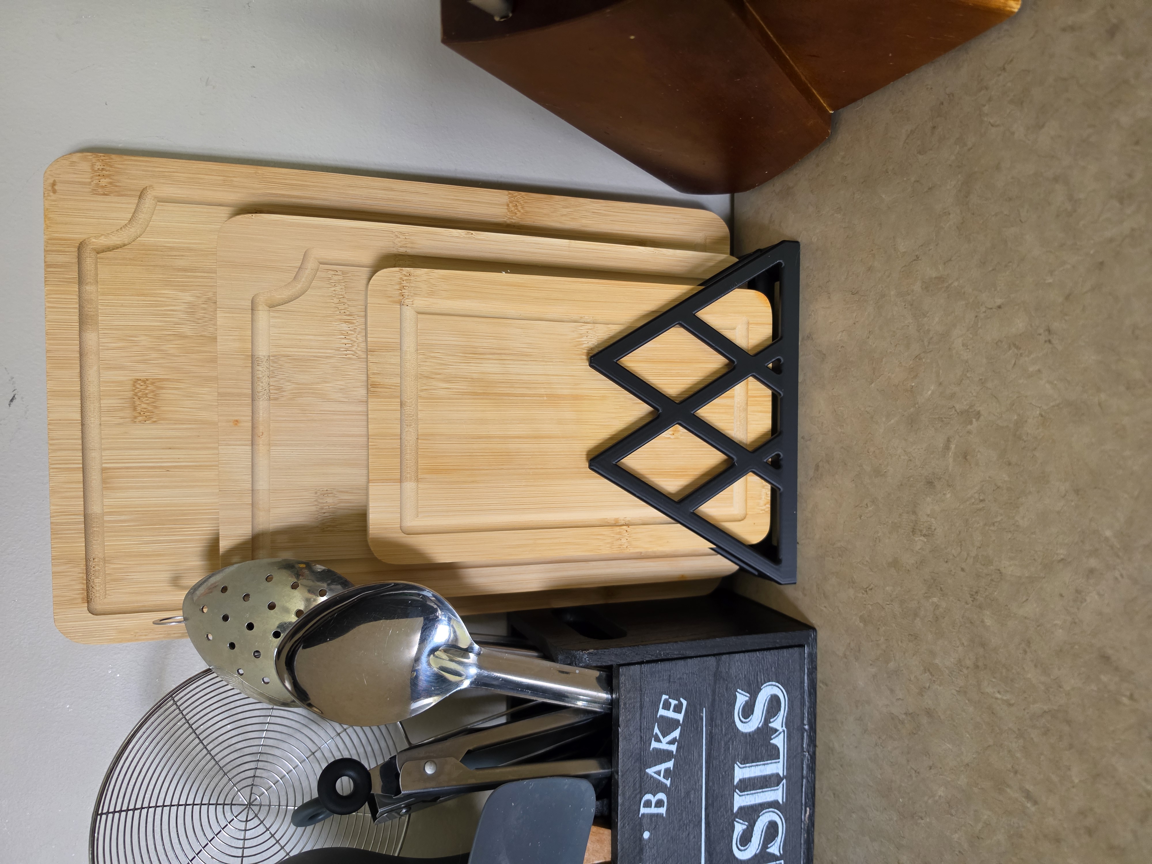 Black diamond-lattice 3D printed cutting board stand holding bamboo boards on a kitchen counter