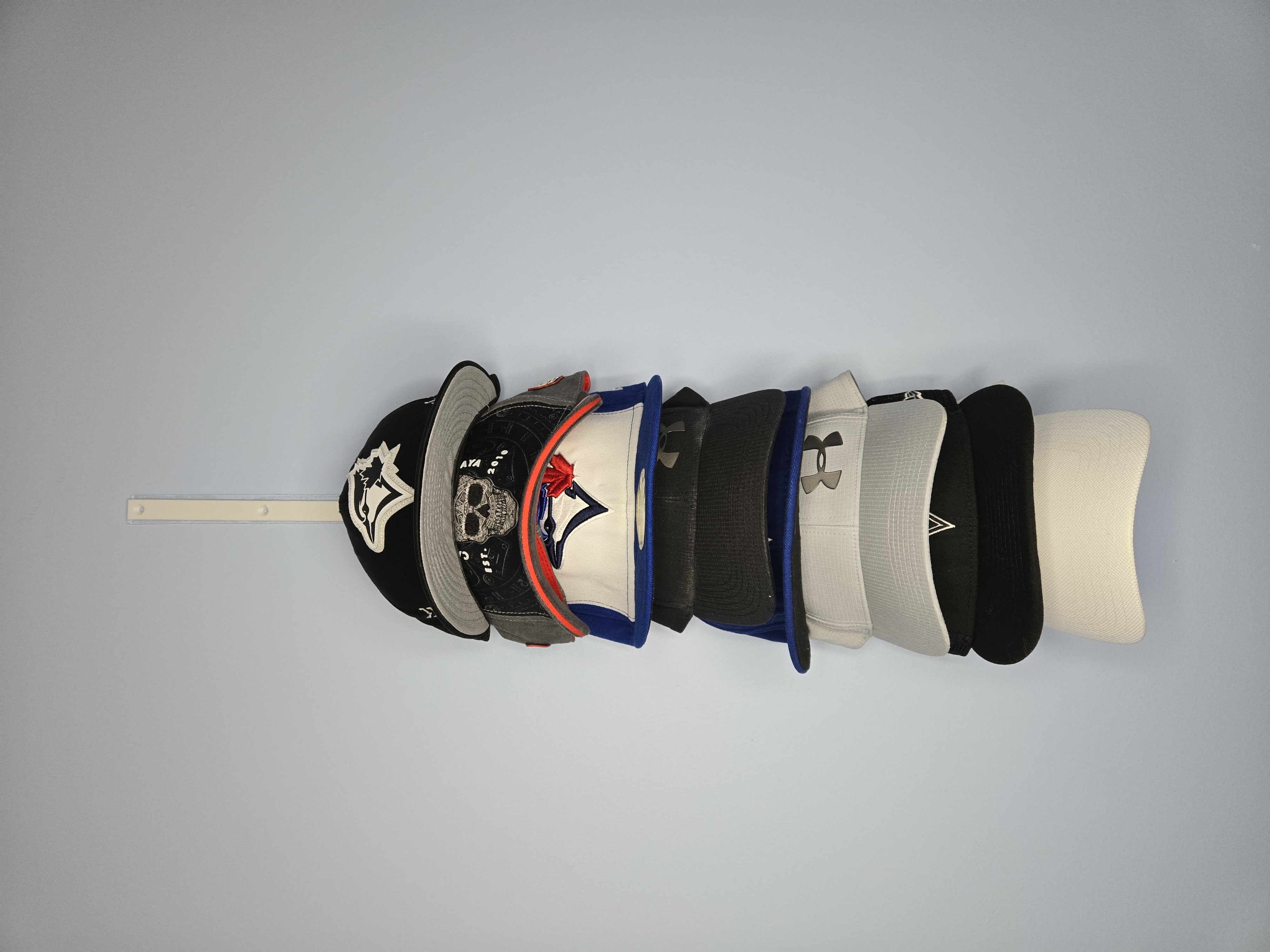 Wall-mounted 3D printed hat rack rail holding a row of baseball caps