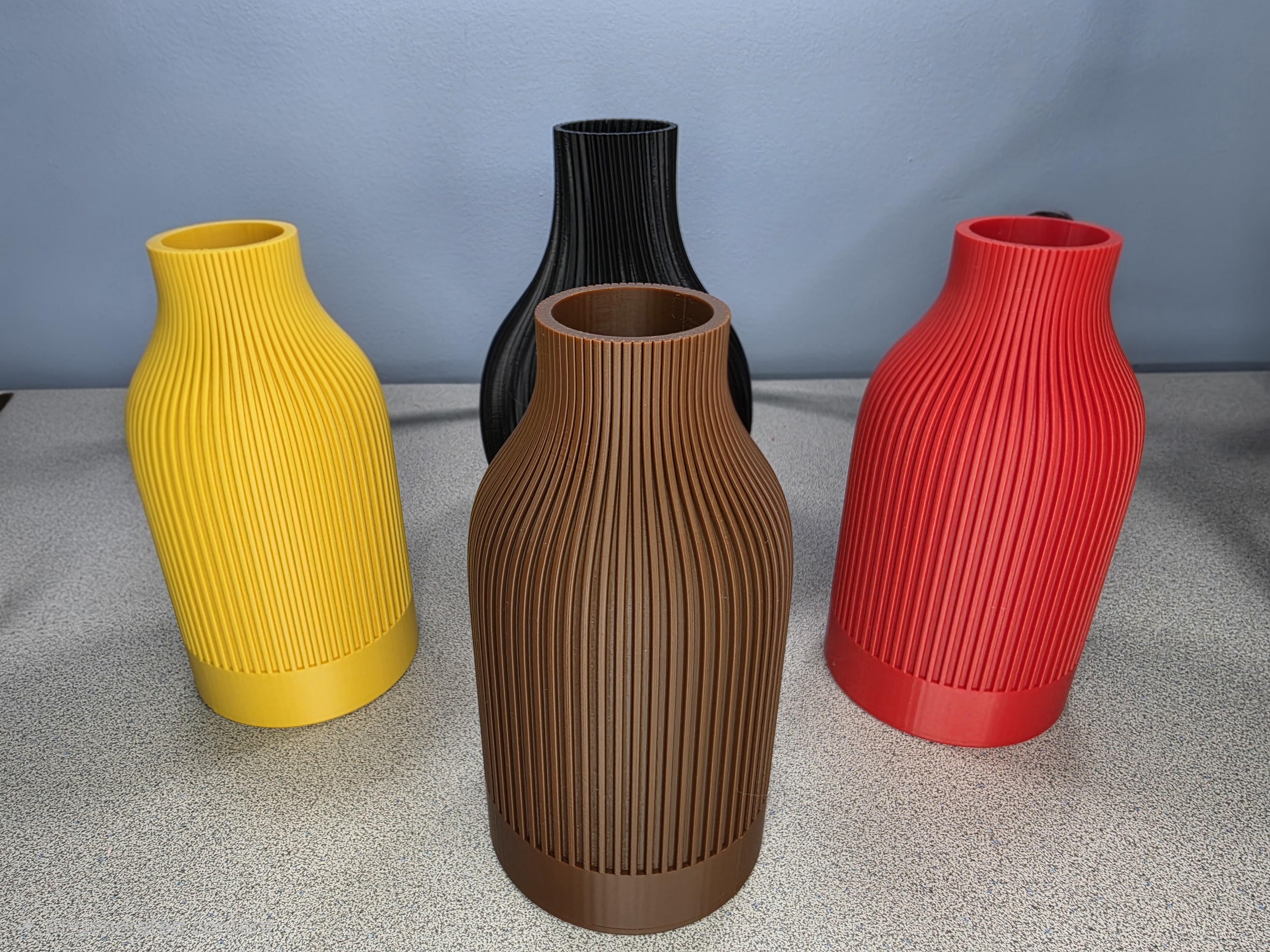 Yellow, black, brown and red 3D printed vases lined up together